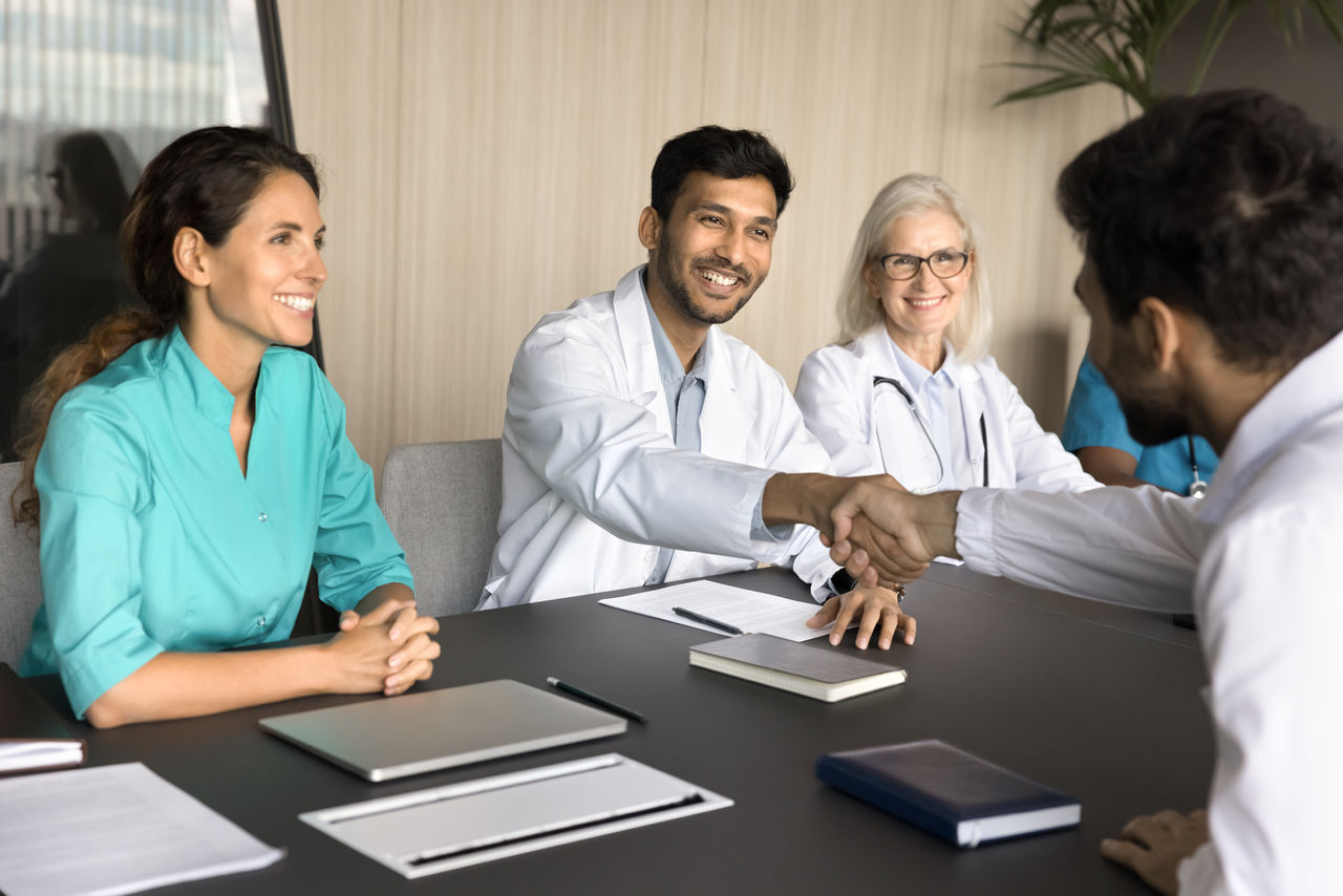 Positive confident chief physician shaking hands with partners, sponsor, hiring new doctor after job interview. Happy recovered patient giving greeting handshake with thank, gratitude
