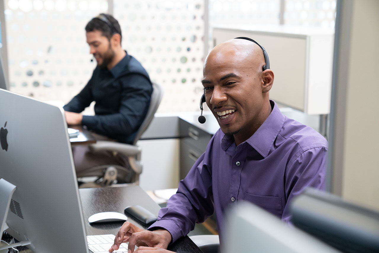 Man smiling in office with headset looking at computer