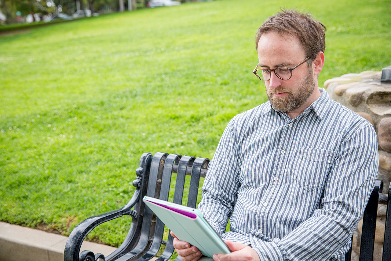 Man sitting on bench looking at tablet outside