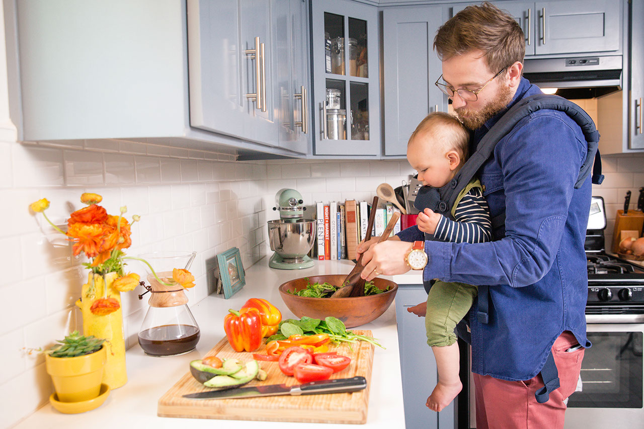 Father prepping food in the kitchen with baby in carrier