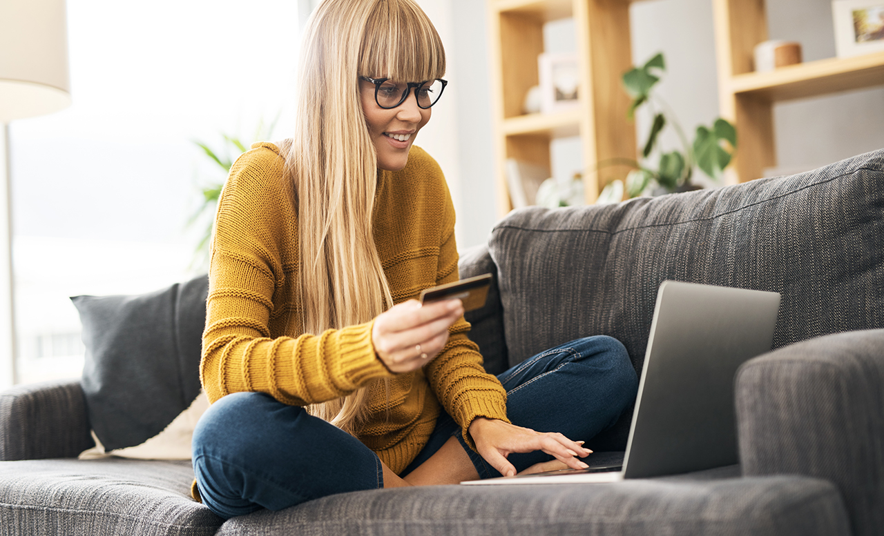 Shot of a young woman using a laptop and credit card on the sofa at home