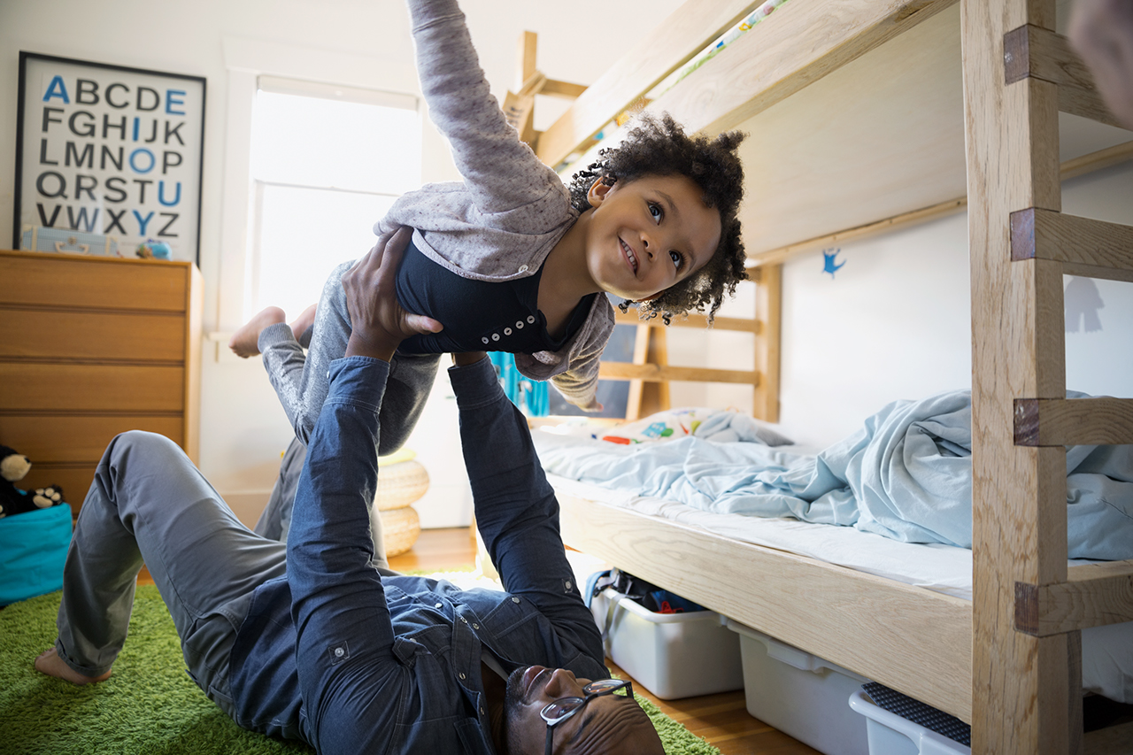 Father lifting flying daughter in bedroom