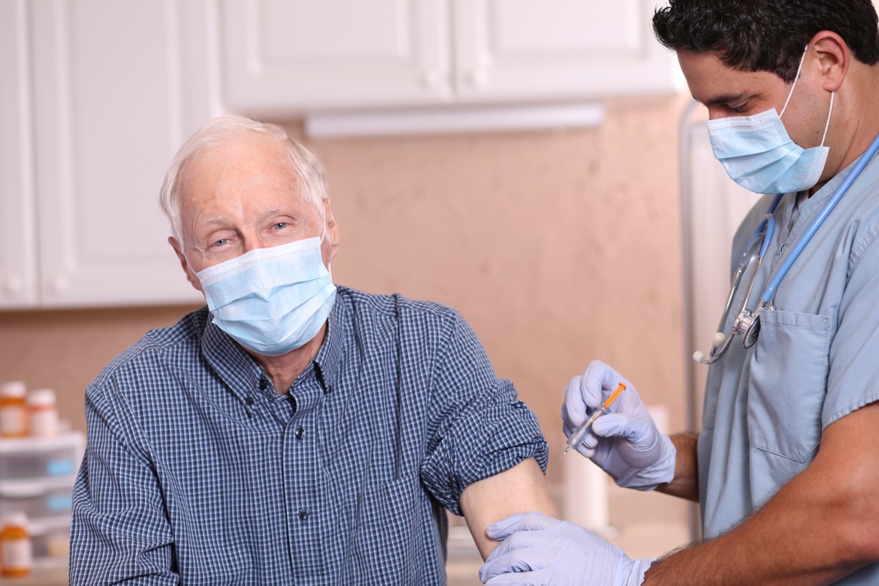 Latin descent doctor or healthcare worker, consultation with senior adult patient in office, hospital, or clinic setting.  He give patient vaccine or medicine injection.  Both wear protective face masks.  Coronavirus, medical exam, consultation.