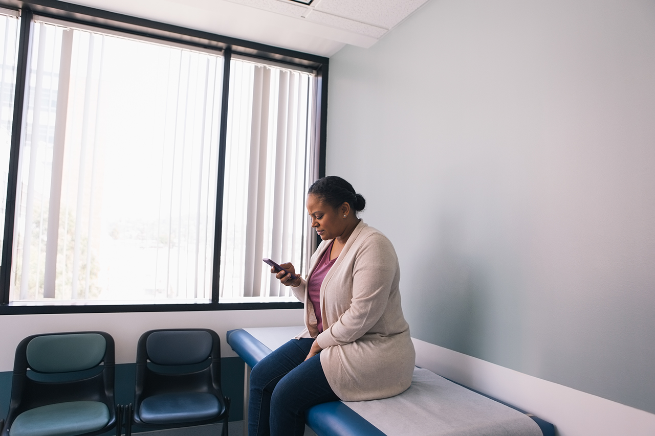 Female patient using mobile phone while sitting in doctors office