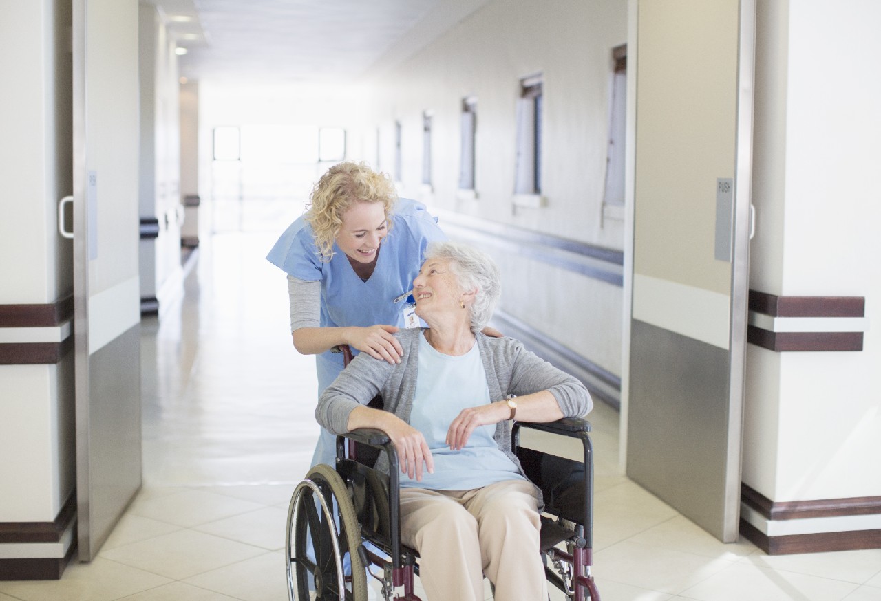 Nurse with aging patient in wheelchair in hospital corridor