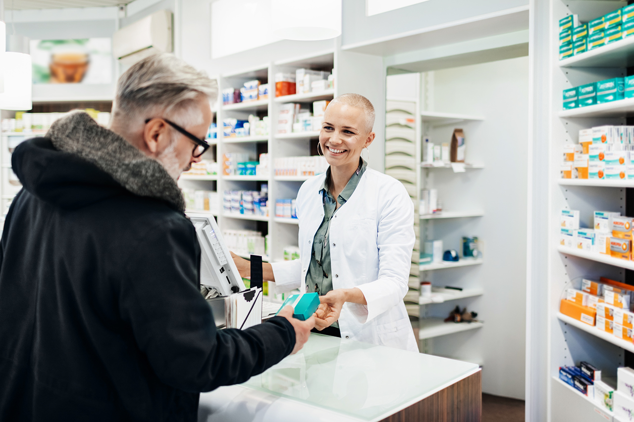 A pharmacist smiling as she serves one of her customers his prescription.